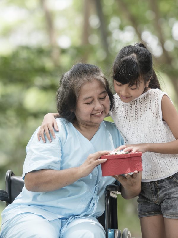 Granddaughter have surprise to grandmother sitting on wheelchair.